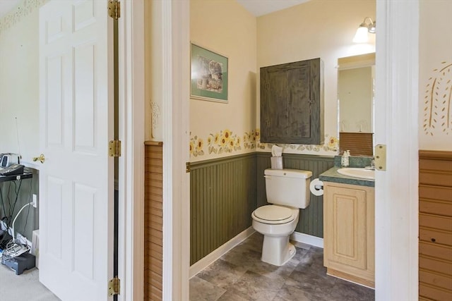 half bathroom with wainscoting, toilet, and vanity