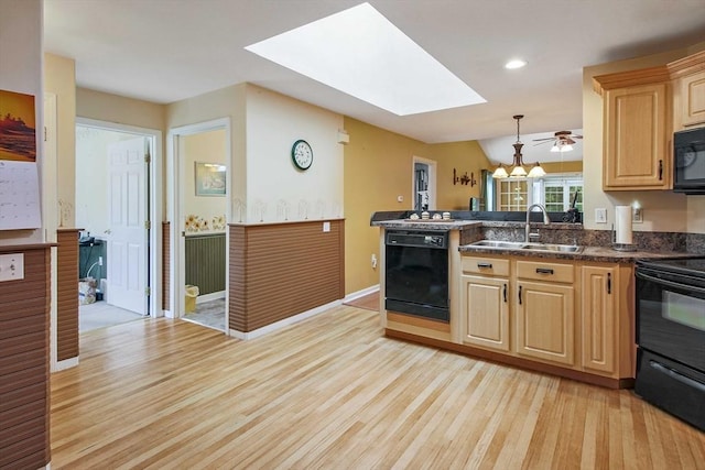 kitchen featuring black appliances, a sink, a skylight, light brown cabinetry, and dark countertops