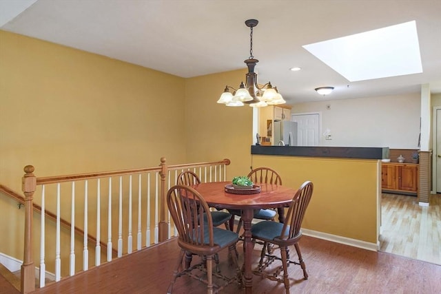 dining room featuring a skylight, light wood-type flooring, a chandelier, baseboards, and recessed lighting