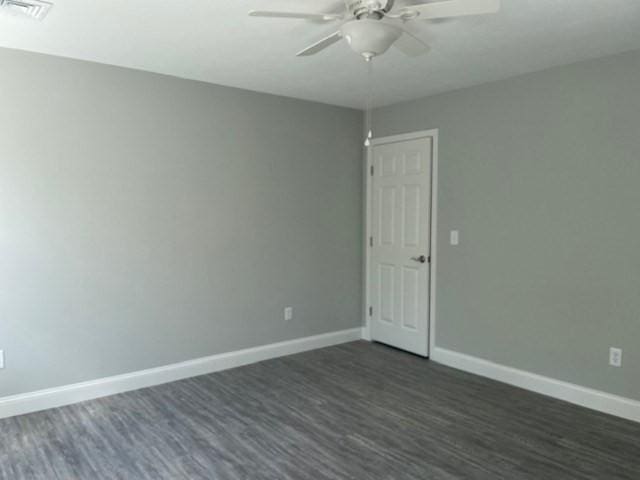 empty room featuring dark wood-type flooring, visible vents, baseboards, and ceiling fan