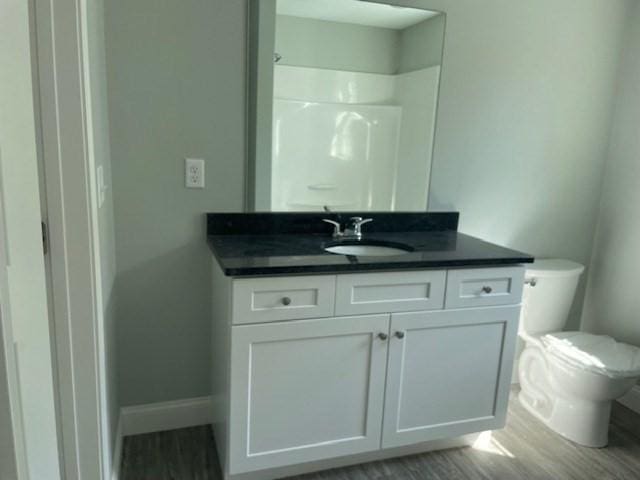 full bathroom featuring toilet, wood finished floors, baseboards, walk in shower, and vanity