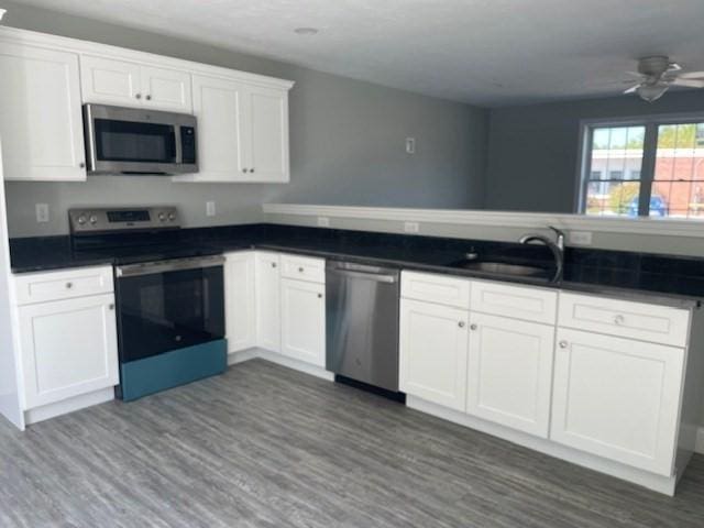 kitchen featuring dark countertops, dark wood-style floors, white cabinets, stainless steel appliances, and a sink