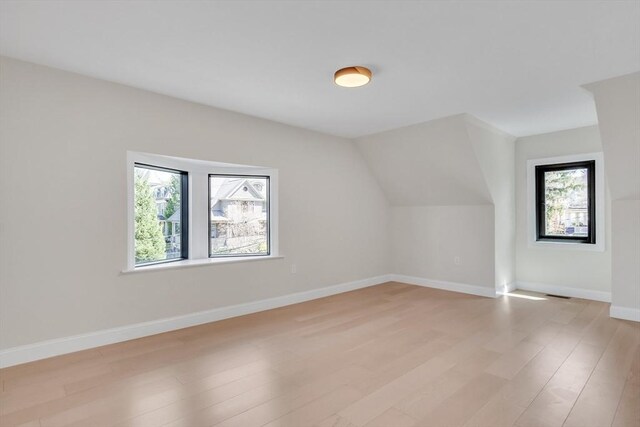 bonus room with baseboards, light wood finished floors, a healthy amount of sunlight, and vaulted ceiling