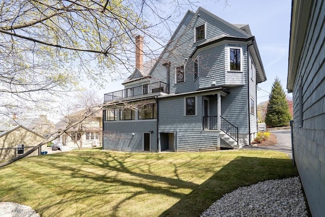rear view of property featuring a yard, a chimney, and a balcony