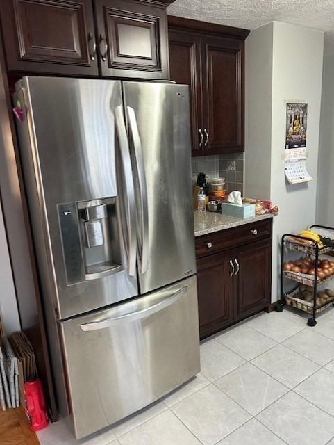 kitchen featuring a textured ceiling, light tile patterned floors, dark brown cabinetry, backsplash, and stainless steel fridge