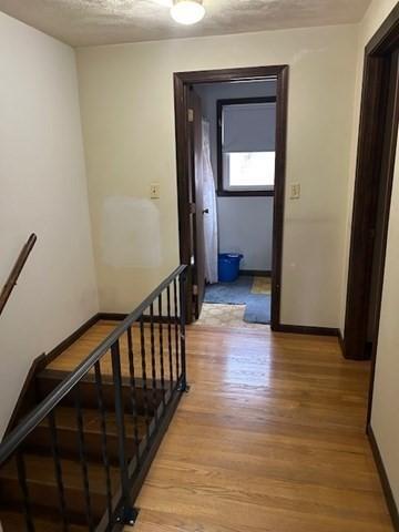 hall with a textured ceiling, light wood-style flooring, an upstairs landing, and baseboards