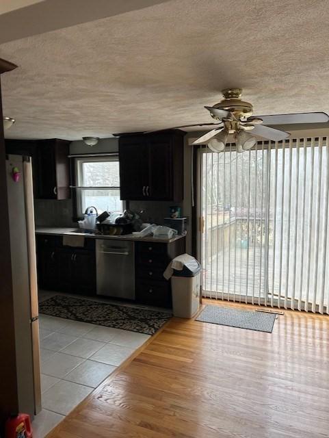 kitchen with appliances with stainless steel finishes, dark cabinets, light wood finished floors, and a textured ceiling