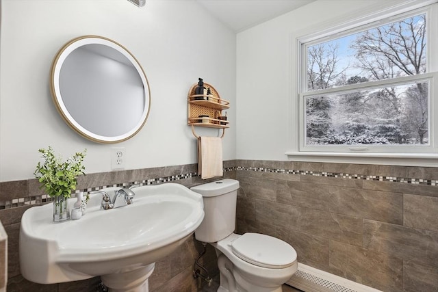 bathroom featuring a baseboard heating unit, sink, tile walls, and toilet