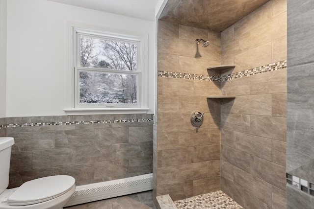 bathroom featuring a tile shower, a baseboard radiator, tile walls, and toilet