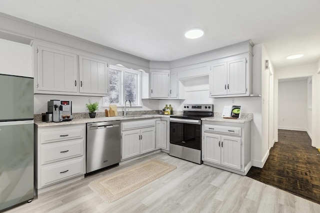 kitchen with stainless steel appliances, white cabinetry, light hardwood / wood-style floors, and sink