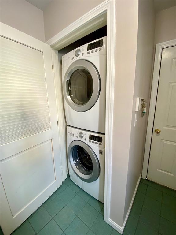 clothes washing area with laundry area, stacked washer and clothes dryer, and tile patterned floors