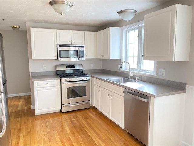 kitchen featuring stainless steel appliances, light countertops, white cabinets, a sink, and light wood-type flooring