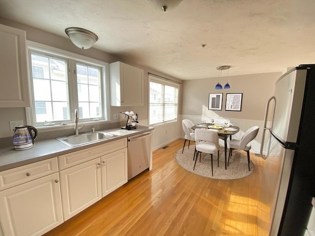 kitchen featuring stainless steel appliances, a sink, decorative light fixtures, and white cabinetry