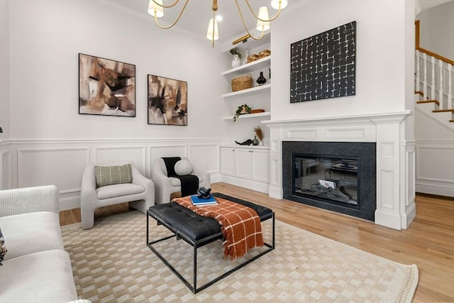 living room with built in shelves, a chandelier, light wood-type flooring, and ornamental molding