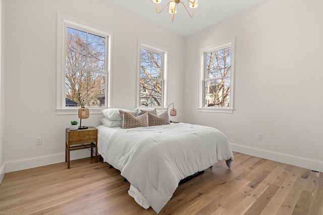 bedroom with a notable chandelier, light wood-type flooring, and multiple windows