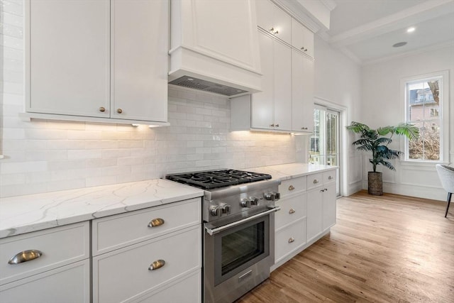 kitchen featuring stainless steel range, light stone counters, backsplash, white cabinets, and light wood-type flooring