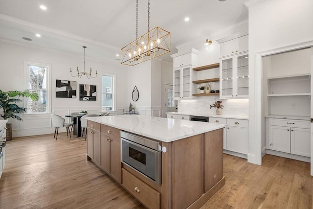 kitchen featuring light stone countertops, light wood-type flooring, white cabinets, a center island, and hanging light fixtures