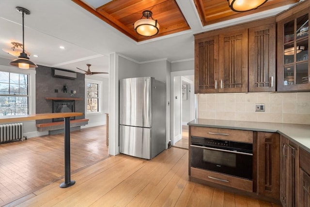 kitchen with a wall mounted AC, light wood-type flooring, stainless steel fridge, radiator, and oven