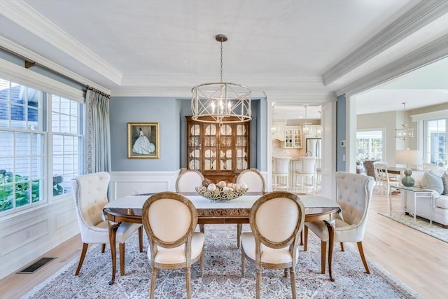 dining area with light wood-type flooring, a chandelier, a wealth of natural light, and ornamental molding