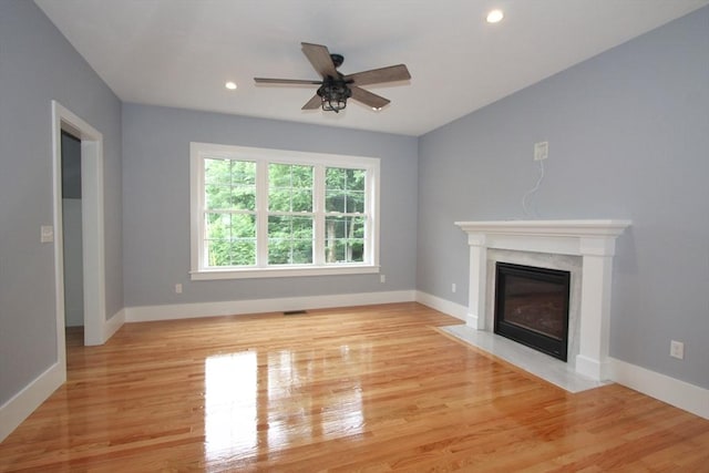 unfurnished living room with ceiling fan, a high end fireplace, and light wood-type flooring