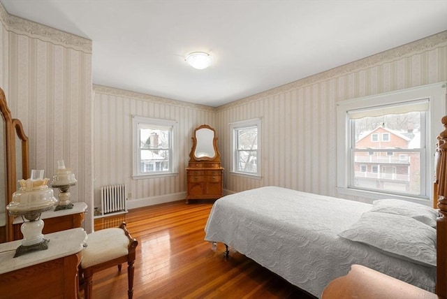 bedroom with wallpapered walls, radiator heating unit, baseboards, and wood finished floors