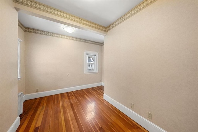 empty room with radiator, hardwood / wood-style flooring, and baseboards