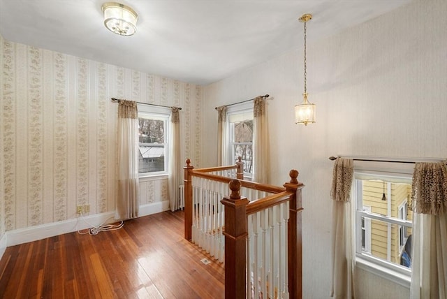 hall featuring baseboards, wood finished floors, an upstairs landing, and wallpapered walls