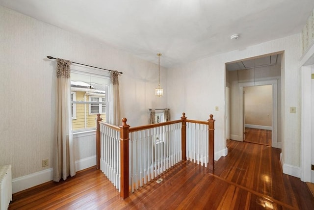 hallway featuring an upstairs landing, baseboards, hardwood / wood-style floors, radiator heating unit, and attic access