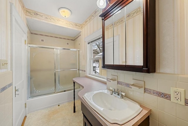 full bath featuring combined bath / shower with glass door, vanity, and tile walls