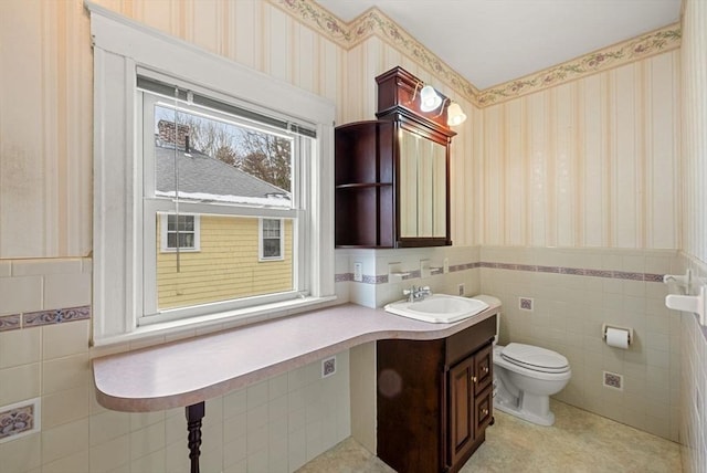 bathroom with toilet, wallpapered walls, tile walls, and wainscoting