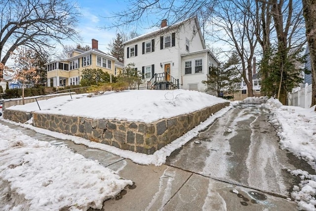 snow covered property with a garage, driveway, and a chimney