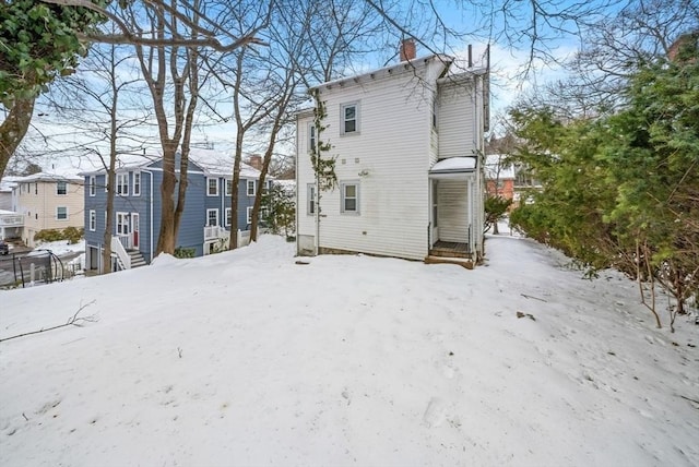 snow covered house with entry steps, a chimney, and a residential view