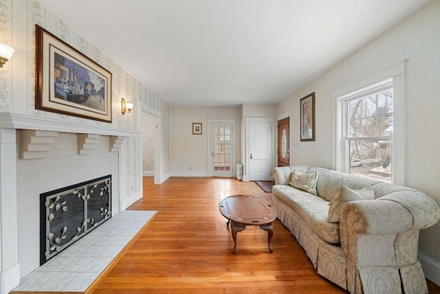 living area featuring light wood-style floors, a tile fireplace, baseboards, and wallpapered walls