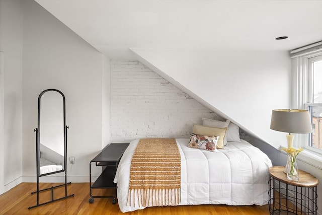 bedroom featuring brick wall and wood finished floors