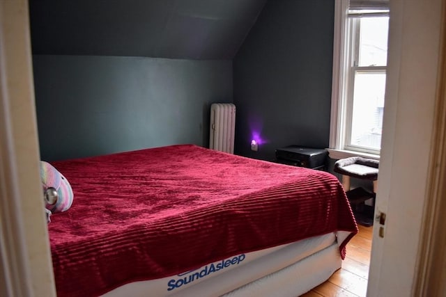 bedroom featuring radiator, wood finished floors, and lofted ceiling