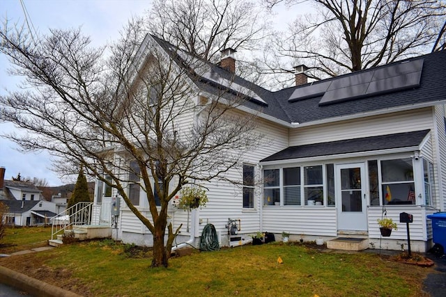 view of home's exterior with a sunroom, a lawn, solar panels, a chimney, and a shingled roof
