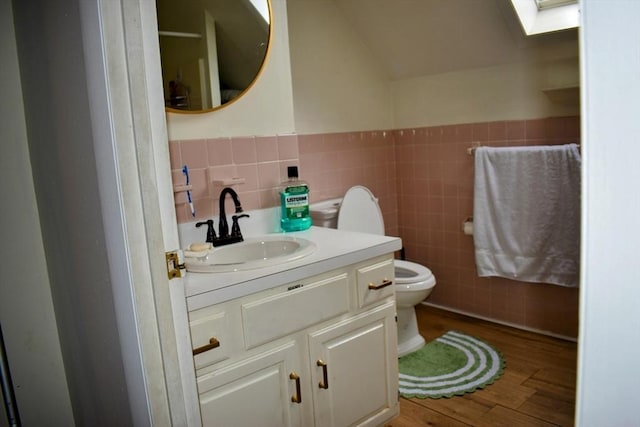bathroom with toilet, tile walls, wainscoting, vanity, and wood finished floors