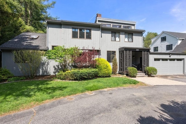 view of front facade with a front lawn, a garage, driveway, and a chimney