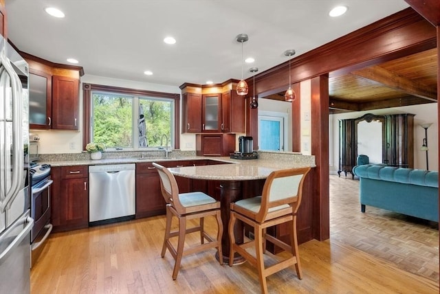 kitchen with stainless steel appliances, a breakfast bar, glass insert cabinets, a peninsula, and hanging light fixtures
