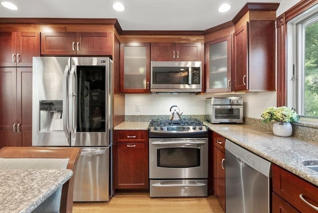 kitchen featuring appliances with stainless steel finishes, recessed lighting, light wood-type flooring, glass insert cabinets, and light stone countertops