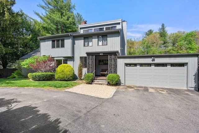 view of front of home with driveway, a chimney, an attached garage, and fence