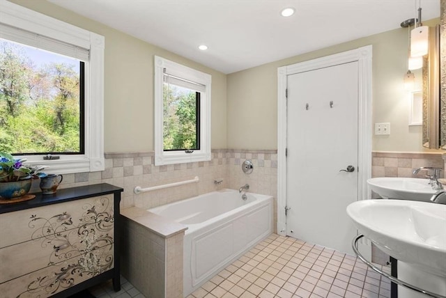 bathroom with tile walls, tile patterned flooring, wainscoting, a bath, and a sink