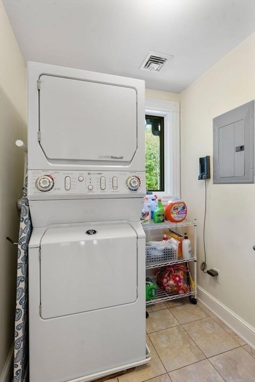 laundry area featuring stacked washer / dryer, electric panel, light tile patterned flooring, and baseboards