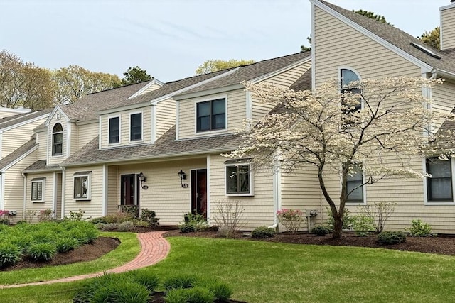 view of front of house with roof with shingles and a front yard