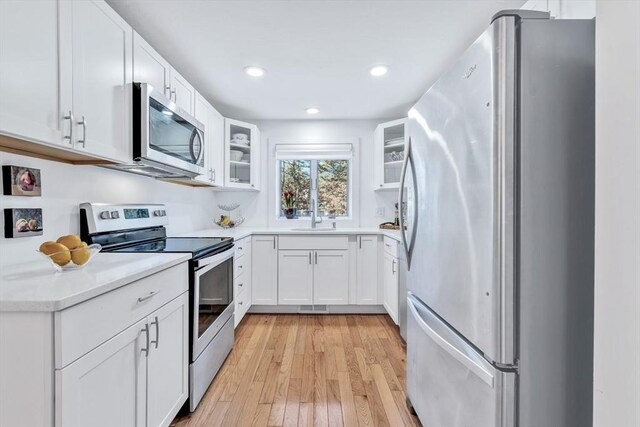 kitchen featuring appliances with stainless steel finishes, light wood-style floors, glass insert cabinets, a sink, and white cabinetry
