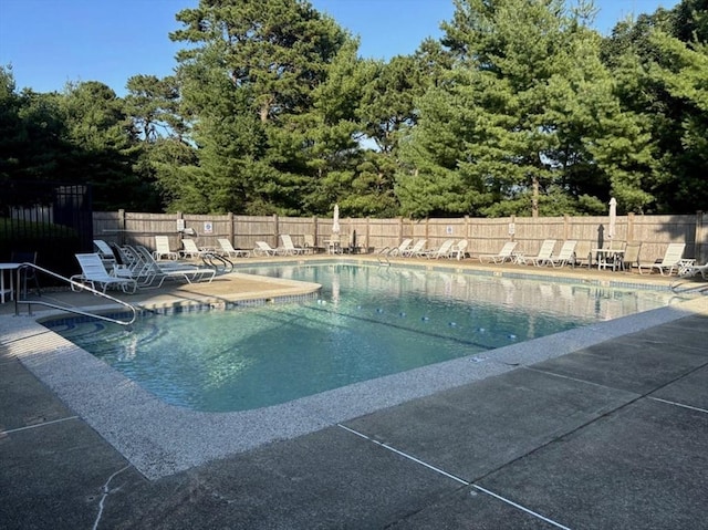 community pool with a patio area, fence, and view of scattered trees