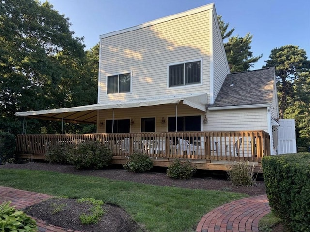 rear view of property featuring a yard, a deck, and roof with shingles