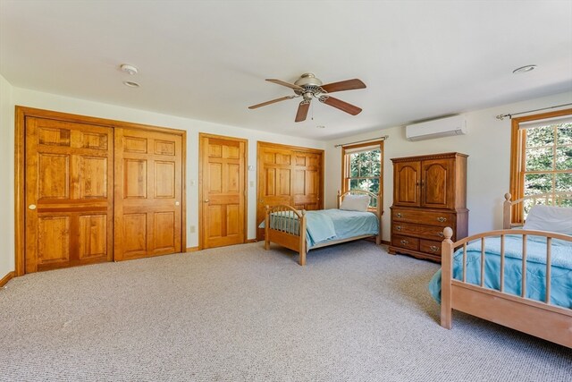 carpeted bedroom with ceiling fan, multiple closets, and an AC wall unit