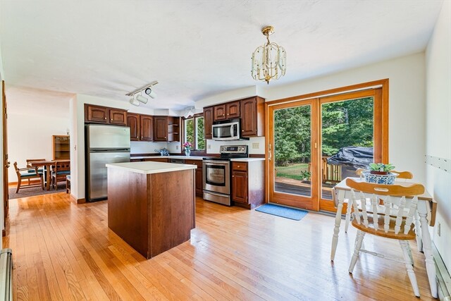 kitchen with appliances with stainless steel finishes, a center island, pendant lighting, and light hardwood / wood-style flooring