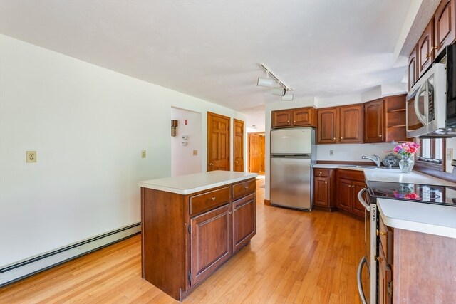 kitchen featuring sink, a kitchen island, a baseboard heating unit, appliances with stainless steel finishes, and light hardwood / wood-style floors